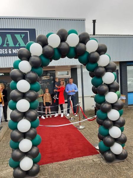 Ballonnenboog in zwart, groen en wit bij een winkelopening met rode loper